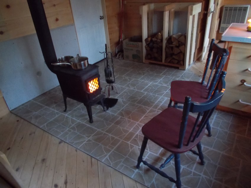 At dusk, the woodstove casts a warm glow on two chairs